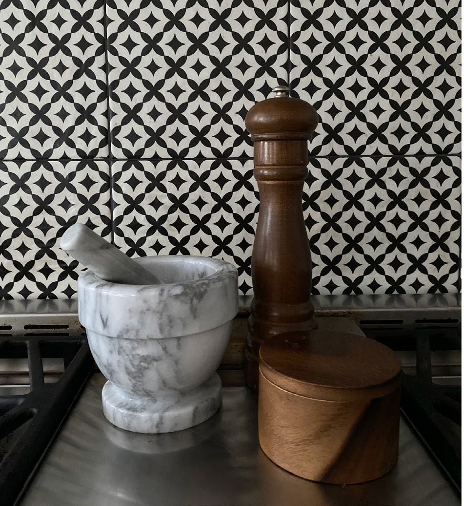 A close-up of a black-and-white patterned tile backsplash with a marble mortar and pestle and a wooden pepper grinder.