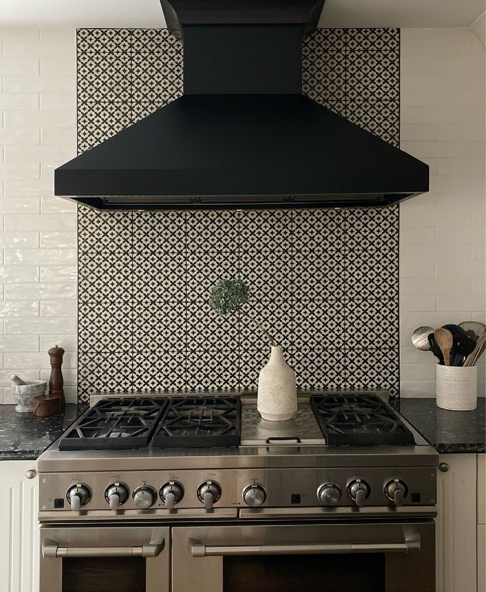 A kitchen range with a black hood and patterned black-and-white tile backsplash.